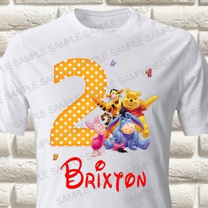 May include: White t-shirt with a yellow and white polka dot number 2, Winnie the Pooh and friends, and the name Brixton in red.