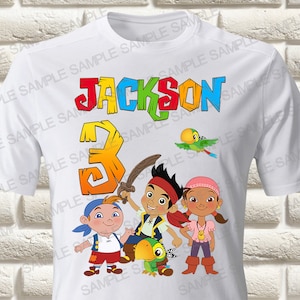 Può includere: Maglietta bianca con una grafica colorata dei personaggi dello show per bambini "Jake e i Pirati del Paese che Non C'è". La grafica include Jake, Izzy e Skully. La maglietta ha anche il nome "Jackson" e il numero "3" in lettere colorate.