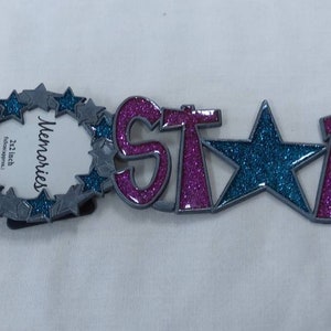 STAR Metal Picture Frame with the word STAR covered in colorful glittery enamel. The picture frame is Circular with little Stars around it.