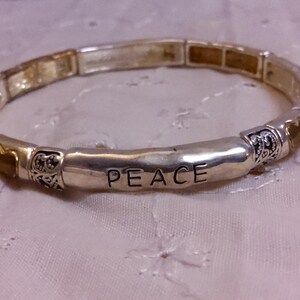May include: A silver bracelet with a charm that says "PEACE" and gold heart charms.