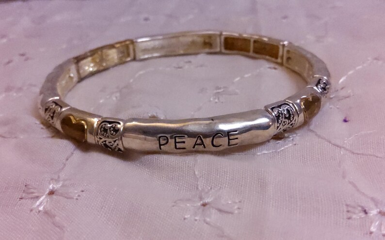 May include: A silver bracelet with a charm that says "PEACE" and gold heart charms.