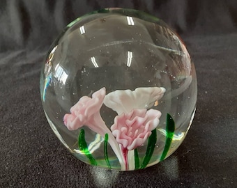 May include: A clear glass paperweight with pink and white flowers and green leaves inside.