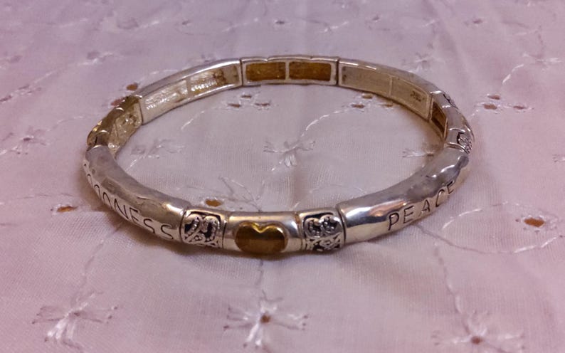 May include: A silver bracelet with a gold heart charm and the words "Peace" and "Goodness" engraved on it.