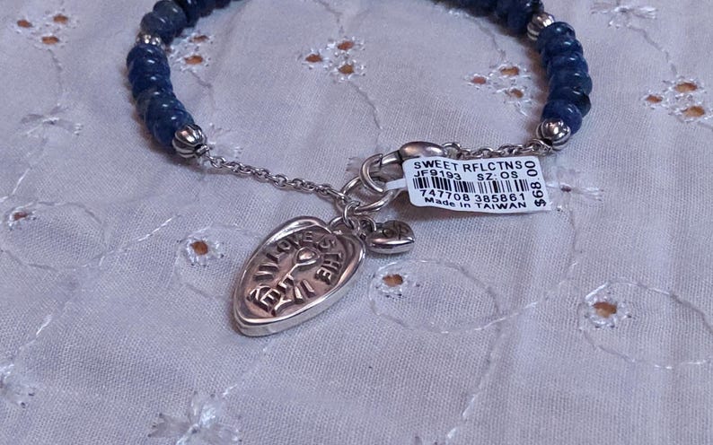 Puede incluir: Una pulsera con cuentas azul oscuro y un dije plateado. El dije es de forma ovalada con las palabras "LOVE THE EARTH" grabadas. Tambi&eacute;n hay un peque&ntilde;o dije de coraz&oacute;n adjunto. La pulsera tiene una etiqueta adjunta con texto.