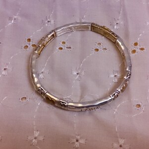 May include: A silver and gold bracelet with a hammered finish and a charm that says "Love".