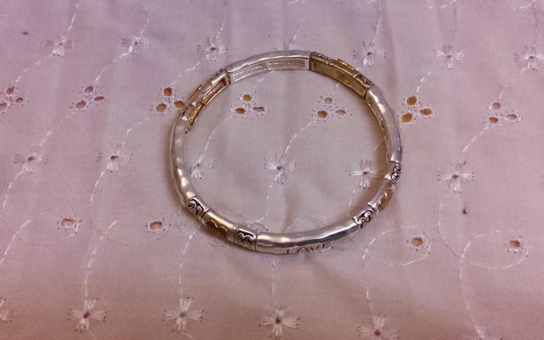 May include: A silver and gold bracelet with a hammered finish and a charm that says "Love".