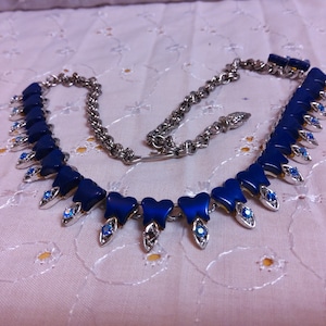 May include: A silver necklace with a chain and a pendant made of blue heart-shaped stones and silver accents. The pendant has a row of blue stones with silver accents.