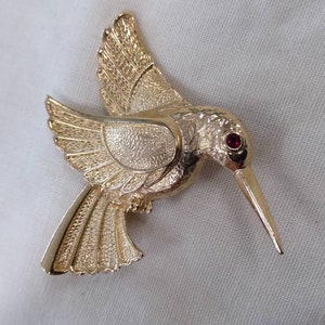 HUMMINGBIRD Goldtone Brooch with Red Rhinestones for the Eyes. Lots of details of the bird crafted into the metal.  No maker&#39;s mark found.