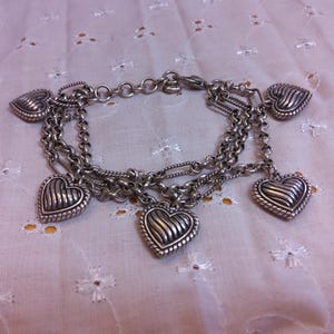 Pu&ograve; includere: Un braccialetto con ciondoli in argento con cinque ciondoli a forma di cuore. I ciondoli sono dettagliati con un design testurizzato e nervato.