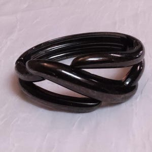 May include: A black, interlocking link bracelet. The bracelet is made of a glossy, dark material and has a chain-like design. The links are smooth and curved, creating a modern and stylish accessory.
