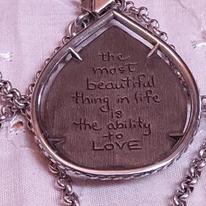 Może przedstawiać: Srebrny naszyjnik z wisiorkiem w kształcie łzy. Wisiorek zawiera wygrawerowany cytat: "najpiękniejszą rzeczą w życiu jest umiejętność KOCHANIA". Łańcuszek naszyjnika ma ogniwowy design.