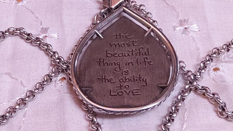 Może przedstawiać: Srebrny naszyjnik z wisiorkiem w kształcie łzy. Wisiorek zawiera wygrawerowany cytat: "najpiękniejszą rzeczą w życiu jest umiejętność KOCHANIA". Łańcuszek naszyjnika ma ogniwowy design.