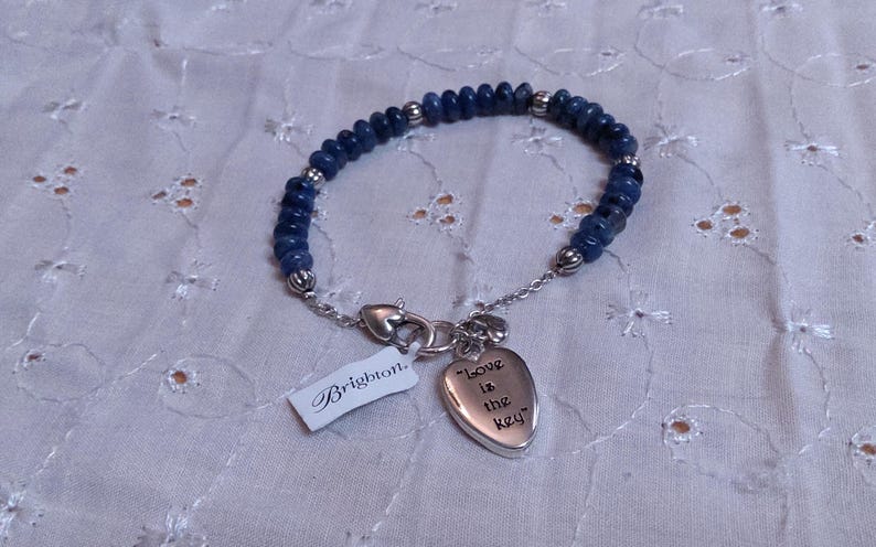 Puede incluir: Una pulsera de cuentas azules con detalles plateados y un dije en forma de coraz&oacute;n con la inscripci&oacute;n "Love is the key". La pulsera tiene un cierre plateado y una etiqueta "Brighton".