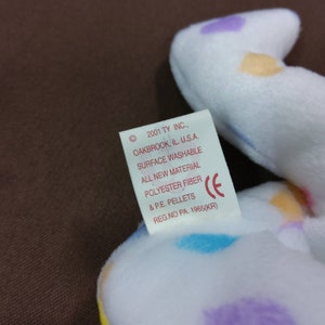 May include: White plush toy with colorful polka dots. The tag reads "2001 TY INC., OAKBROOK, IL. U.S.A. SURFACE WASHABLE ALL NEW MATERIAL POLYESTER FIBER & P.E. PELLETS REG.NO PA. 1965(KR)"