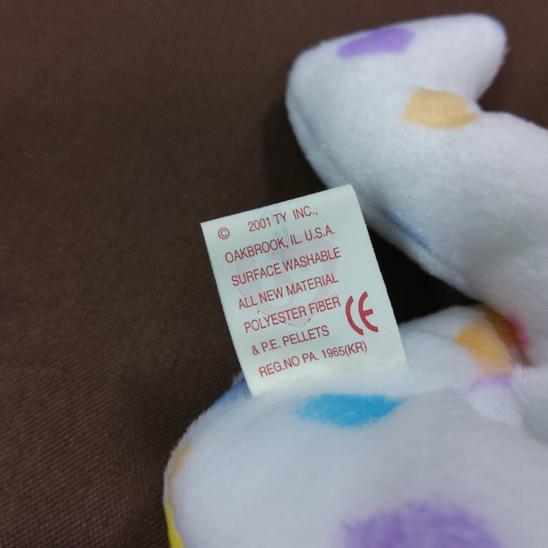 May include: White plush toy with colorful polka dots. The tag reads "2001 TY INC., OAKBROOK, IL. U.S.A. SURFACE WASHABLE ALL NEW MATERIAL POLYESTER FIBER & P.E. PELLETS REG.NO PA. 1965(KR)"