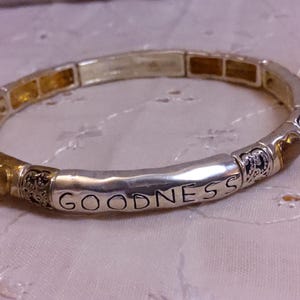 May include: Silver and gold tone stretch bracelet with the word "GOODNESS" engraved on one of the links.