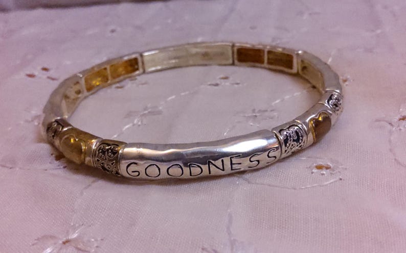 May include: Silver and gold tone stretch bracelet with the word "GOODNESS" engraved on one of the links.