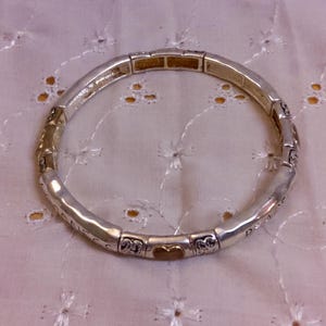May include: A silver bracelet with a gold heart charm. The bracelet is made of small, linked pieces with decorative details.