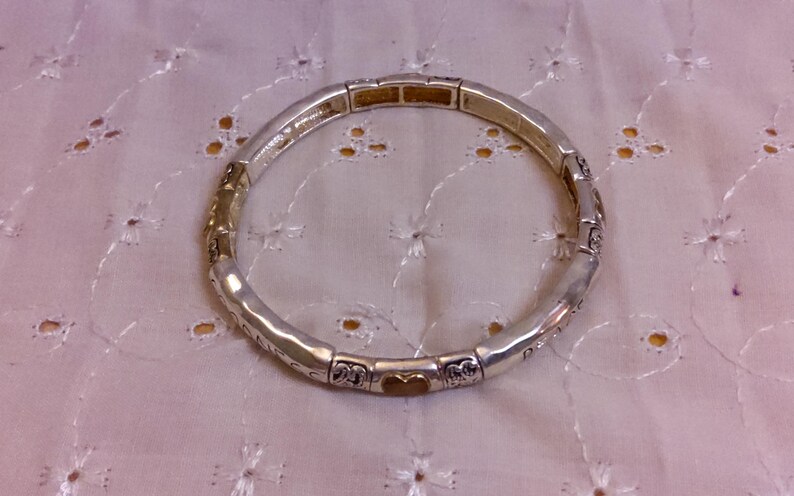 May include: A silver bracelet with a gold heart charm. The bracelet is made of small, linked pieces with decorative details.