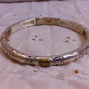 May include: A silver bracelet with a gold heart charm and the words "Peace" and "Love" engraved on it.