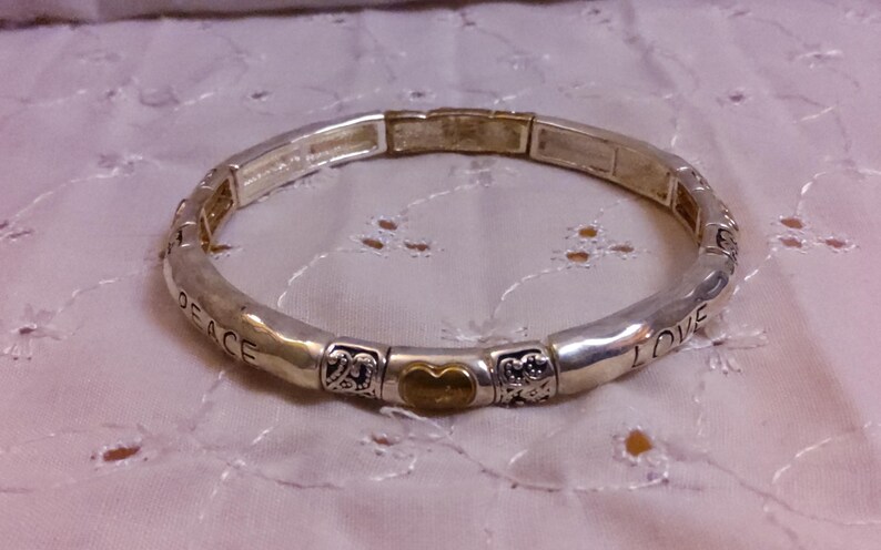 May include: A silver bracelet with a gold heart charm and the words "Peace" and "Love" engraved on it.