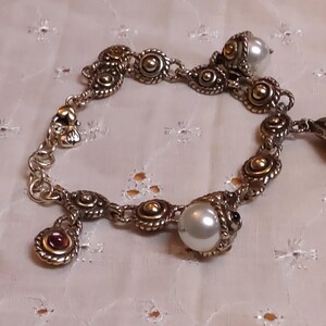 May include: Silver-toned bracelet with gold accents, featuring round and oval links. The bracelet includes pearl and gemstone charms. The design incorporates ornate detailing and a vintage aesthetic, suitable for jewelry enthusiasts.