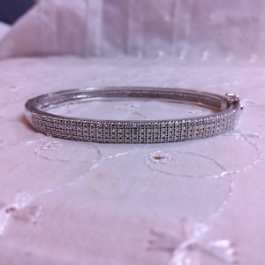 May include: A silver bangle bracelet with a row of small, clear diamonds.