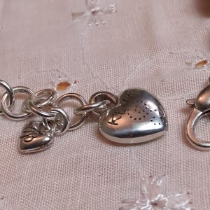 May include: Silver-toned bracelet with heart-shaped charms and a lobster clasp. The bracelet features a series of round links and decorative beads. The heart charms have a textured surface with small cut-out designs.
