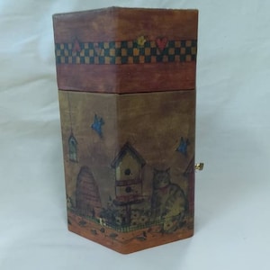 May include: A hexagonal wooden box with a painted design of a cat, birdhouses, and a beehive. The box has a hinged lid and a brass latch.
