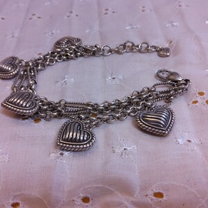 Pu&ograve; includere: Un braccialetto d'argento con pi&ugrave; fili di catena e cinque ciondoli a forma di cuore. I cuori hanno un design testurizzato e nervato.