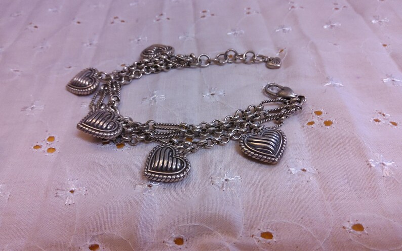 Pu&ograve; includere: Un braccialetto d'argento con pi&ugrave; fili di catena e cinque ciondoli a forma di cuore. I cuori hanno un design testurizzato e nervato.