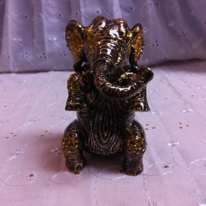 May include: A small, black and gold elephant figurine with rhinestones. The elephant is sitting with its trunk curled up.