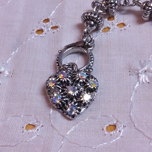 May include: A silver heart charm with clear iridescent rhinestones. The charm is attached to a silver chain with a silver clasp.
