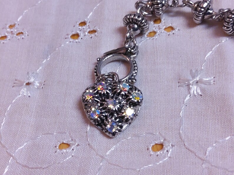 May include: A silver heart charm with clear iridescent rhinestones. The charm is attached to a silver chain with a silver clasp.