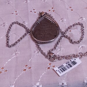 Może przedstawiać: Srebrny naszyjnik z wisiorkiem w kształcie łzy. Wisiorek ma napis i jest przymocowany do łańcuszka. Widoczna jest metka z ceną. Naszyjnik spoczywa na białej, wzorzystej powierzchni.