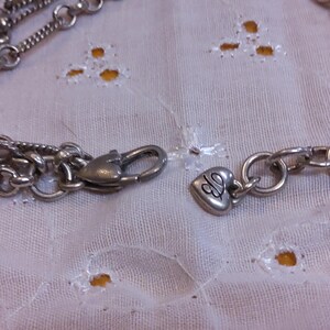 Pu&ograve; includere: Una collana a catena d'argento con un ciondolo a forma di cuore e una chiusura che dice "CJ".