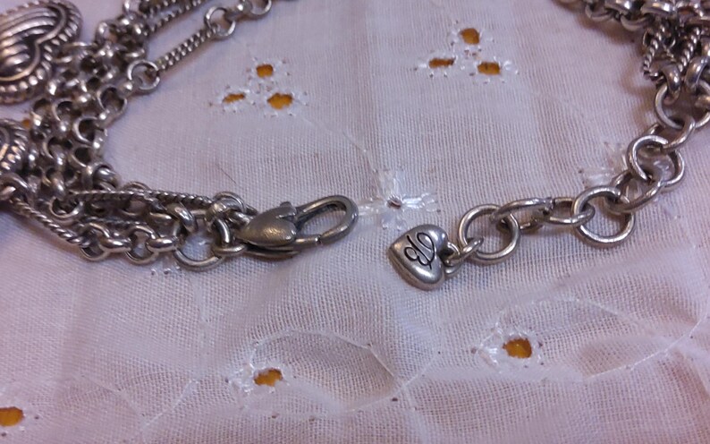 Pu&ograve; includere: Una collana a catena d'argento con un ciondolo a forma di cuore e una chiusura che dice "CJ".