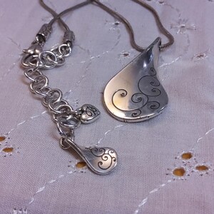 May include: A silver necklace with a teardrop-shaped pendant. The pendant has a swirl design and is attached to a silver chain.