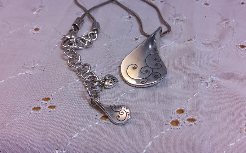 May include: A silver necklace with a teardrop-shaped pendant. The pendant has a swirl design and is attached to a silver chain.