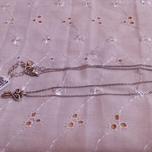 Op de afbeelding: Zilverkleurige ketting met een sleutelhanger. De sleutelhanger heeft een hartvormig ontwerp. De ketting ligt op een witte stof met een bloemenpatroon. Een prijskaartje is bevestigd.