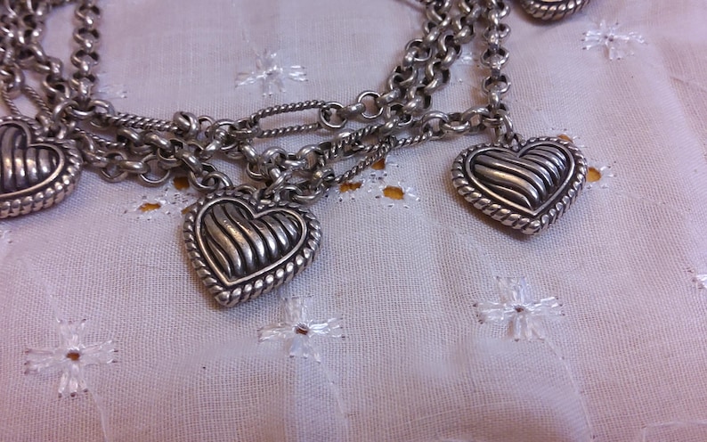 Pu&ograve; includere: Una collana a catena d'argento con pi&ugrave; ciondoli a forma di cuore. Ogni cuore ha un design testurizzato e nervato.