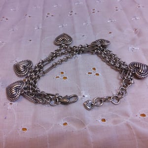 Pu&ograve; includere: Braccialetto in argento con pi&ugrave; ciondoli a forma di cuore. Il braccialetto &egrave; composto da pi&ugrave; catene e ha una chiusura a moschettone.