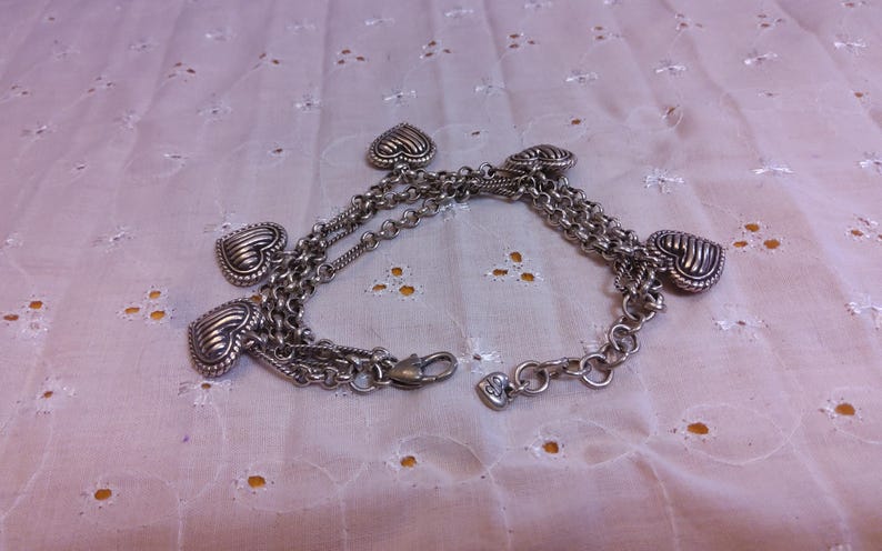 Pu&ograve; includere: Braccialetto in argento con pi&ugrave; ciondoli a forma di cuore. Il braccialetto &egrave; composto da pi&ugrave; catene e ha una chiusura a moschettone.