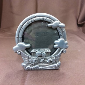 May include: Silver-toned picture frame shaped like a boat with the words "Let it Rain" around the frame. The frame has a small window for a photo and features animal figurines on the boat.