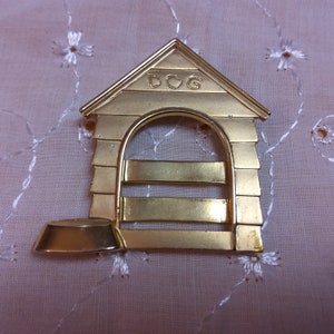 May include: Gold-colored metal dog house ornament with the word "DOG" on the roof and a separate bowl at the bottom.