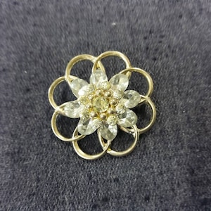 Puede incluir: Un broche de flor de tono dorado con diamantes de imitación transparentes y un centro de cuentas doradas más pequeñas.