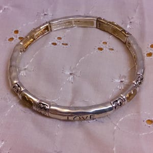 May include: A silver bracelet with a gold accent and the word "LOVE" engraved on it.