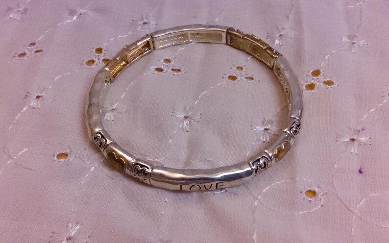May include: A silver bracelet with a gold accent and the word "LOVE" engraved on it.