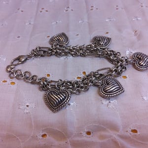 Pu&ograve; includere: Un braccialetto con ciondoli in argento con pi&ugrave; catene e cinque ciondoli a forma di cuore. I ciondoli hanno un design testurizzato e nervato.