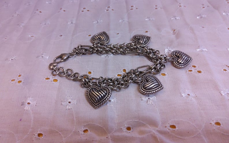 Pu&ograve; includere: Un braccialetto con ciondoli in argento con pi&ugrave; catene e cinque ciondoli a forma di cuore. I ciondoli hanno un design testurizzato e nervato.